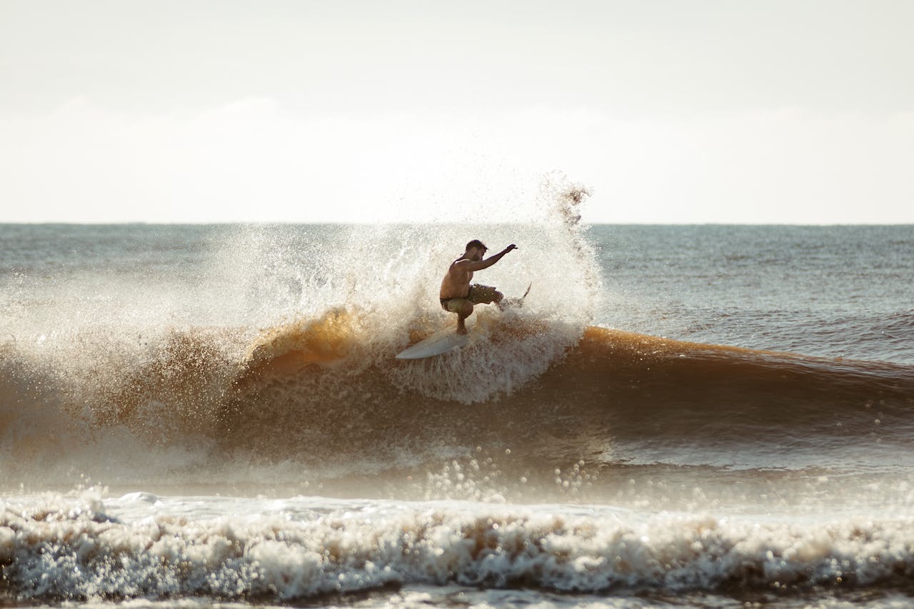 A dynamic action shot of a surfer catching a wave under a clear sky.