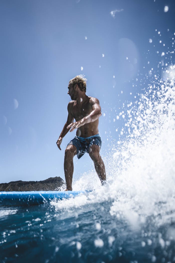 Dynamic shot of a man surfing with vibrant blue skies and splashing waves, capturing a thrilling summer adventure.