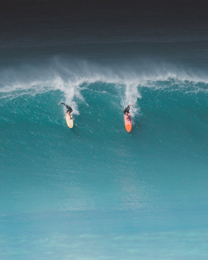 Two surfers ride massive waves in Hawaii, capturing the thrill of ocean sports.