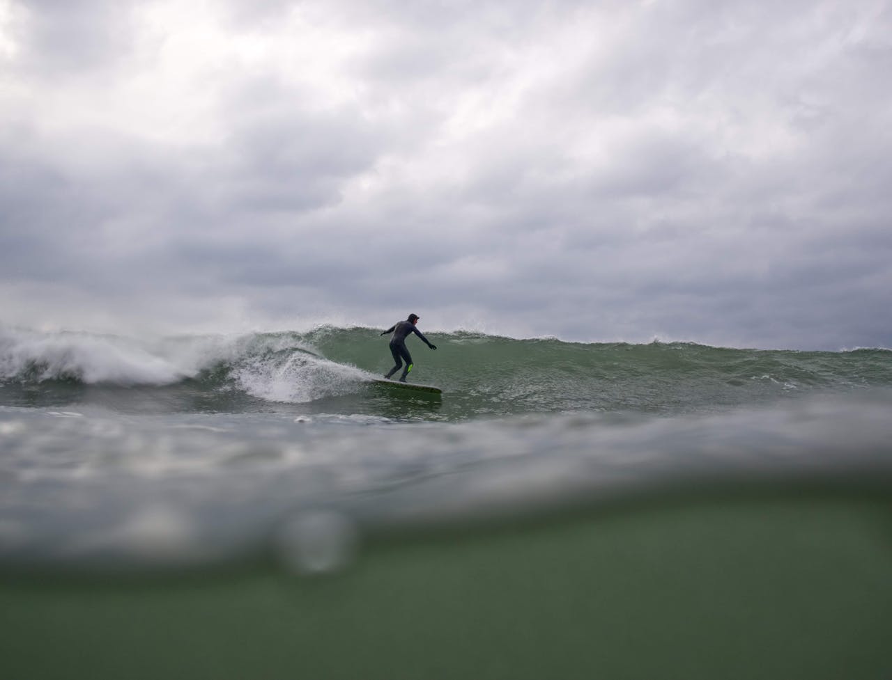 A surfer skillfully rides a wave under a cloudy sky, capturing the thrill of ocean sports.