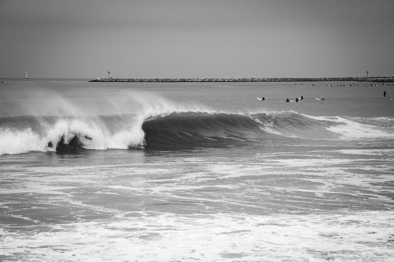 Monochrome seascape capturing ocean waves and surfers near a breakwater.